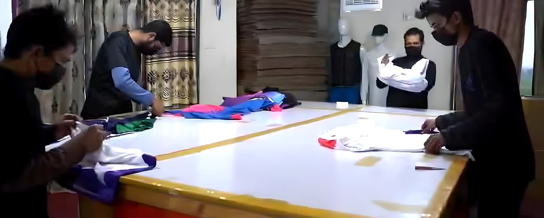 Team marking and cutting garment panels on a long cutting table
