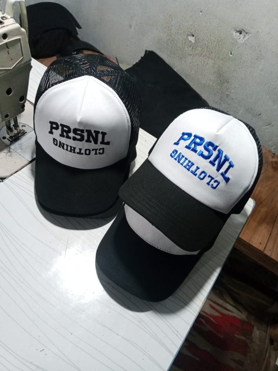 Trucker caps with printed fronts next to an industrial sewing machine